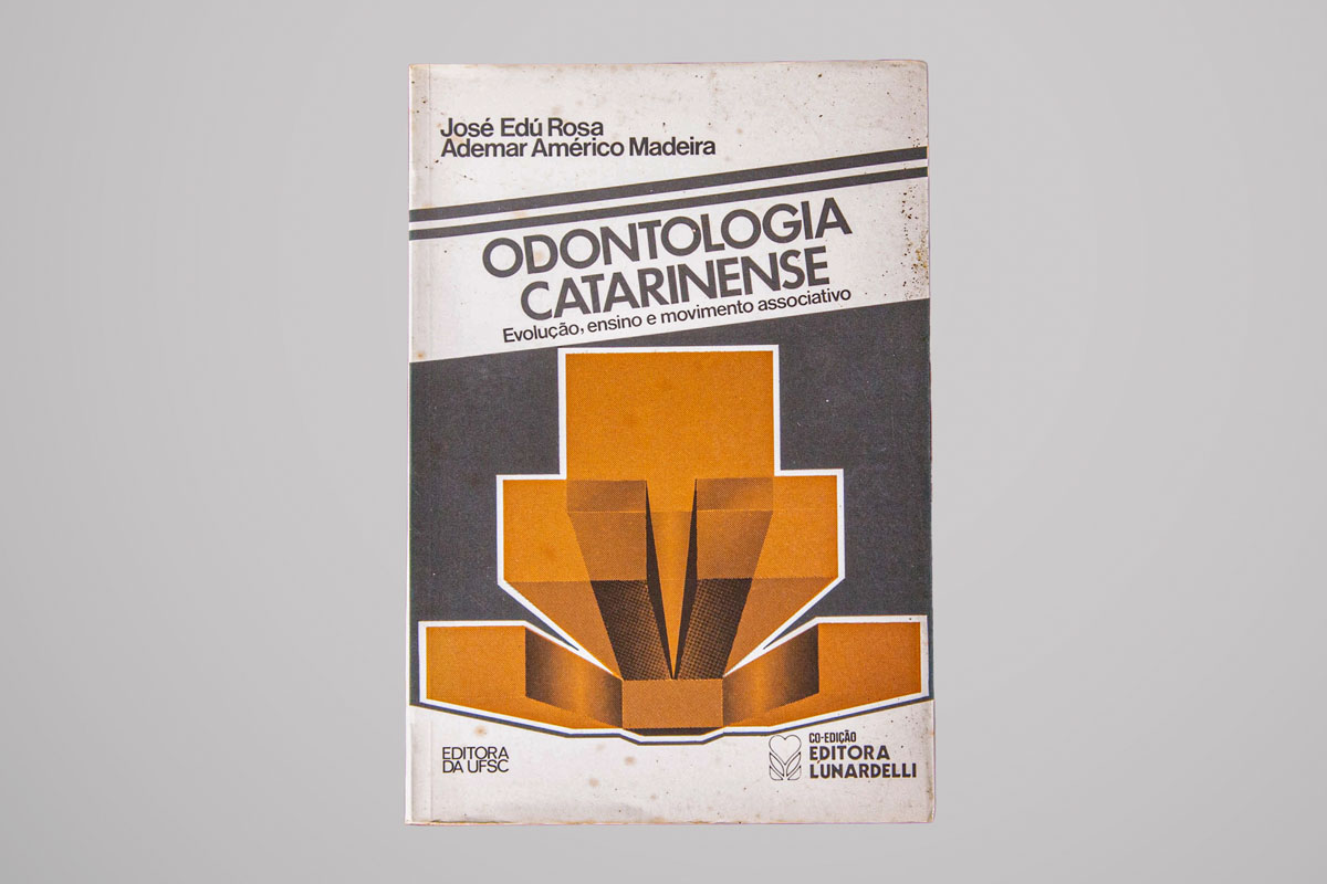 Capa do livro "Odontologia Catarinense: Evolução, ensino e movimento associativo", de José Edú Rosa e Ademar Américo Madeira. O design da capa é simples, com um gráfico geométrico em tons de marrom e laranja. Os nomes dos autores e editoras aparecem na parte inferior.